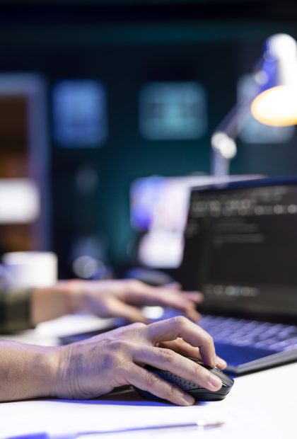 Closeup of person coding at his desk, typing on digital laptop and using a mouse, managing database systems. Working independently, an individual excels in cyber security and machine learning.